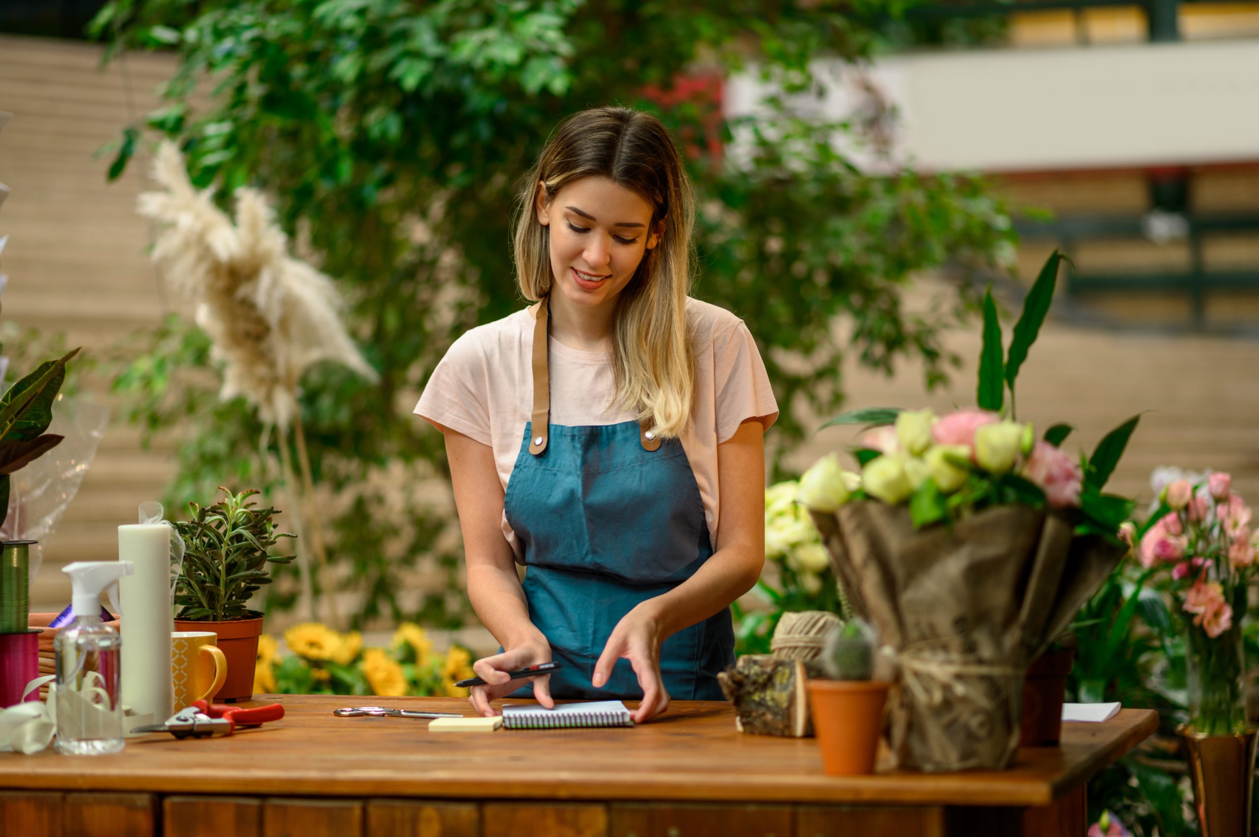 Portrait of florist writing in notebook while leaning against counter while surrounded with flowers and plants in a flower shop