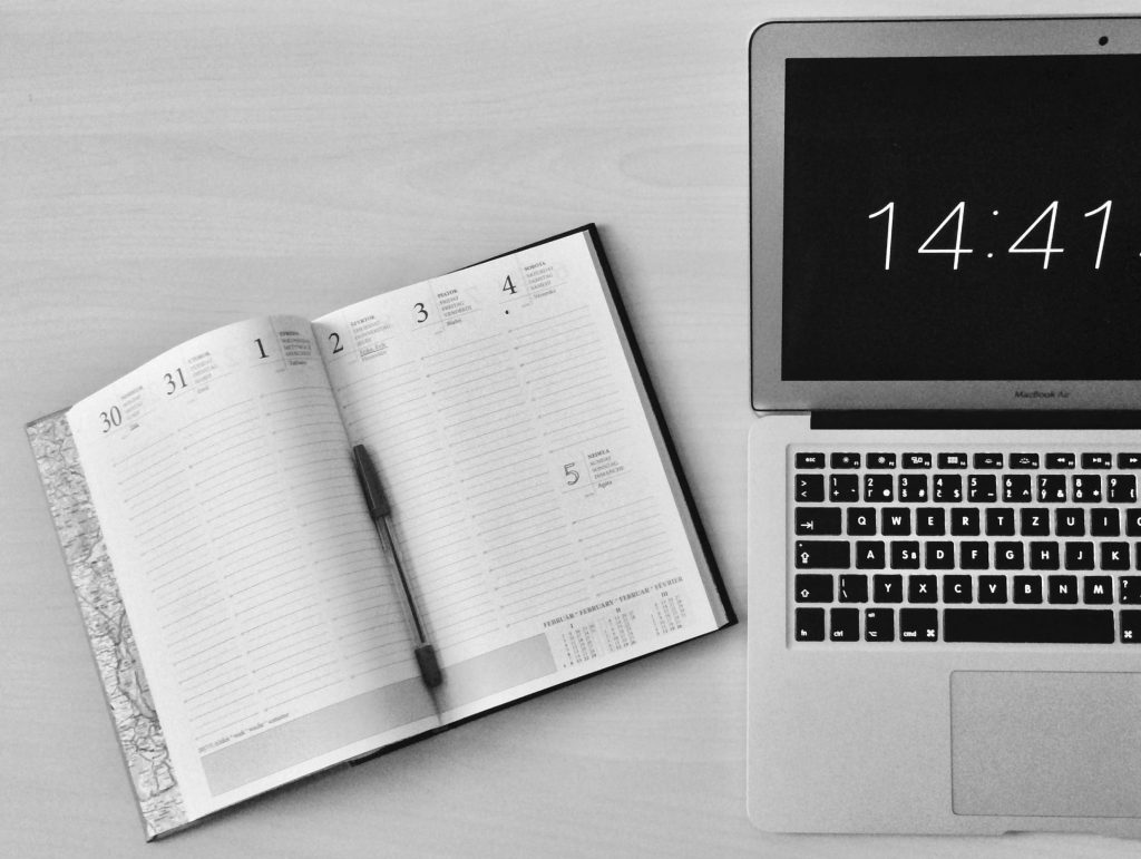 macbook and a ballpen inside a calendar planner