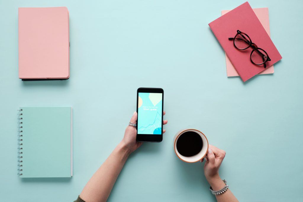 top view shot of an accountant holding a cellphone and a coffee beside it